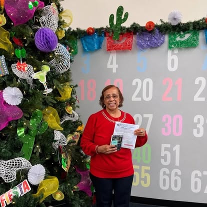 Woman holding a gift by a decorated Christmas tree